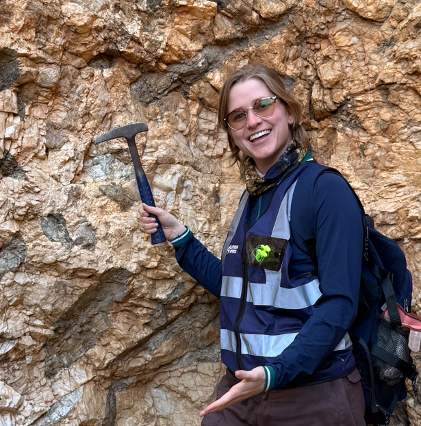 Geologist holding a rock hammer in front of a pegmatite